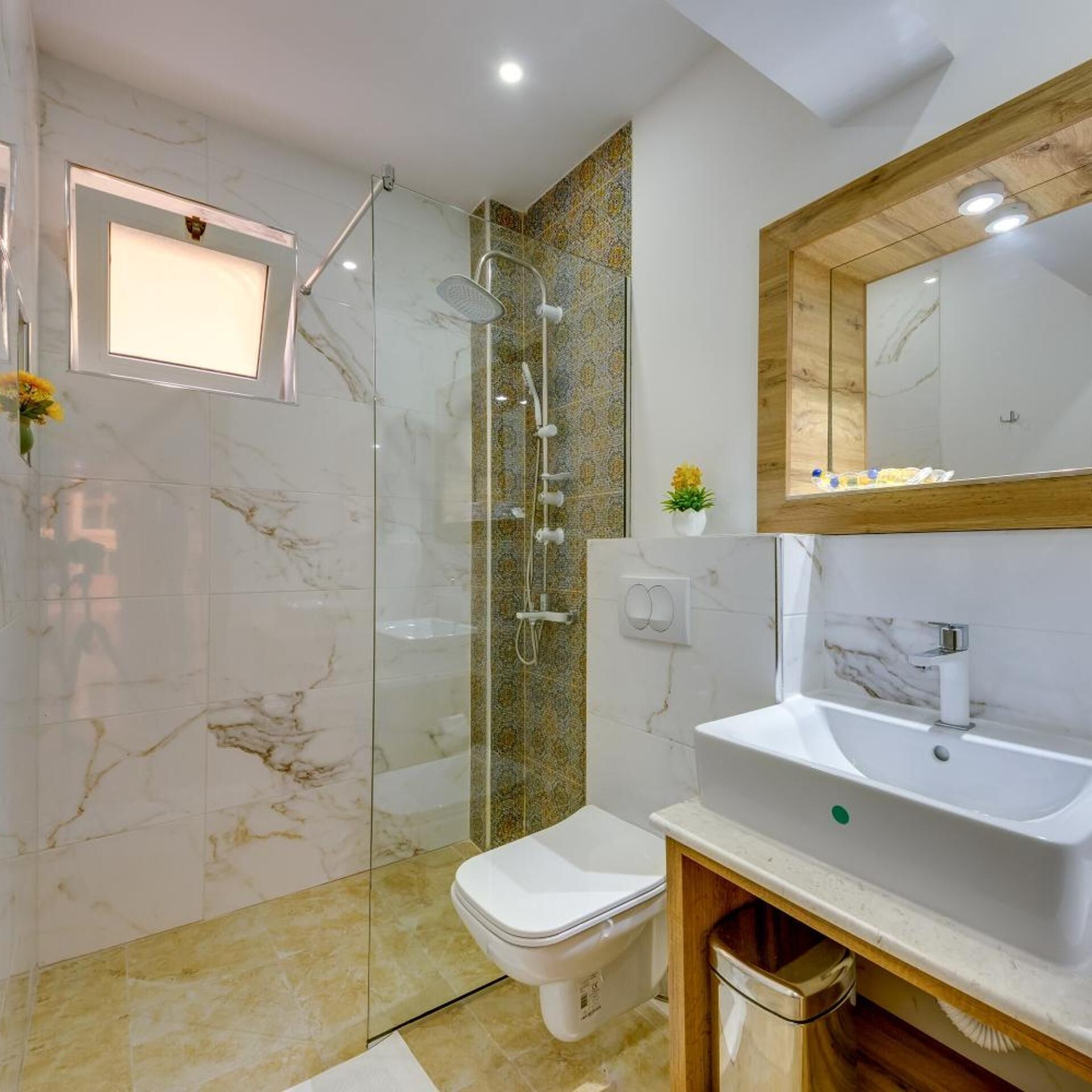 A modern bathroom with a glass-enclosed shower, a white toilet, a sink with a mirror, and a small plant on the countertop.