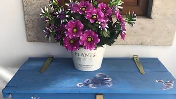 A blue chest of drawers with floral decorations, a potted plant with purple flowers, and a window in the background.