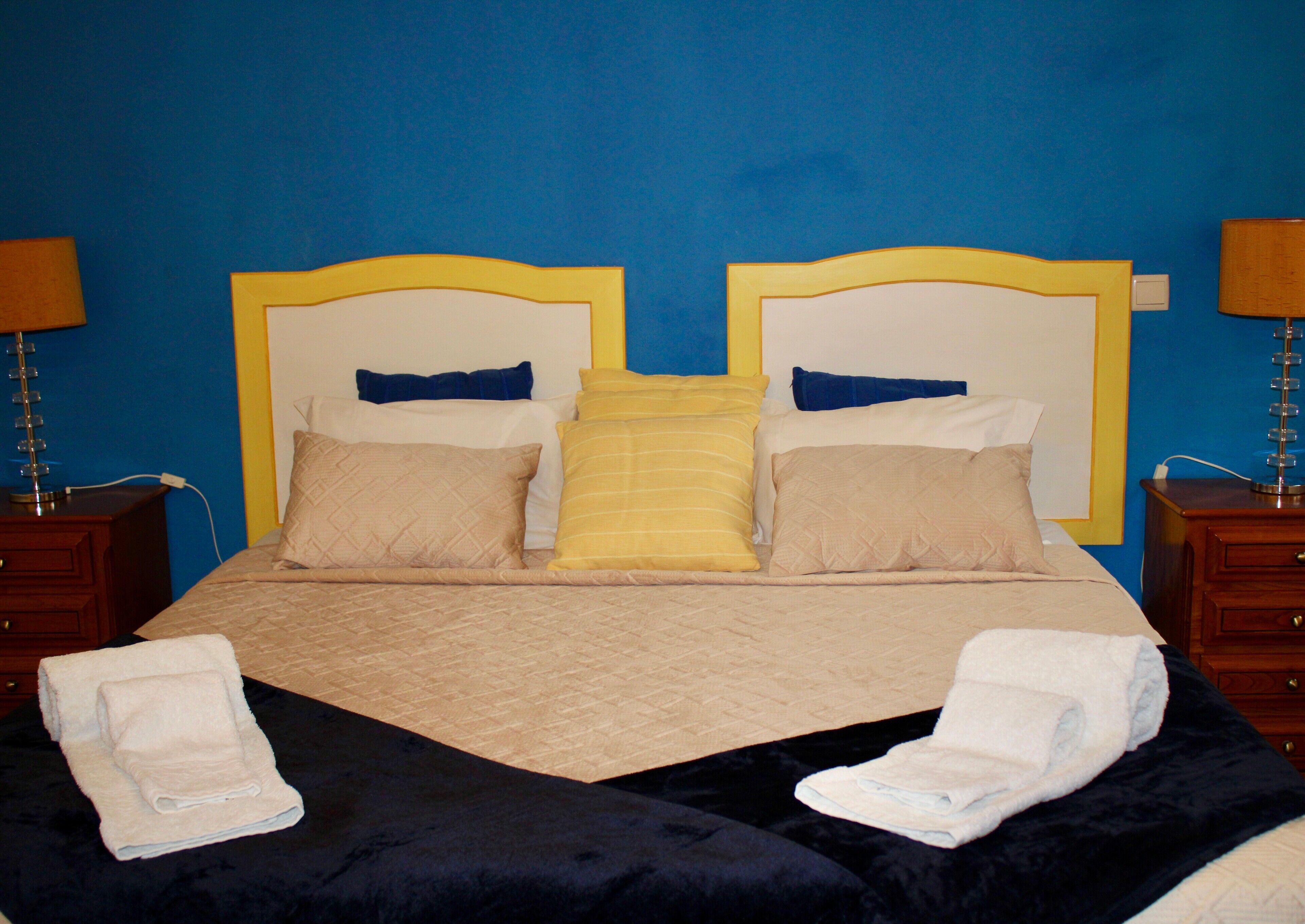 A bed with a quilted cover, two bedside tables with lamps, and towels on the bed.