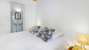 Een slaapkamer met een bed, twee kussens, een bedlampje, een spiegel en een wastafel.