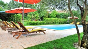 Zona de piscina con sillas de descanso y sombrillas.