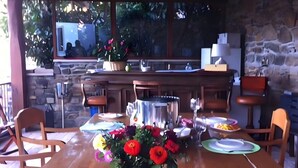 Una mesa de comedor de madera con un jarrón de flores rojas, rodeada de sillas, en una habitación con pared de piedra y ventana con vistas a la vegetación.