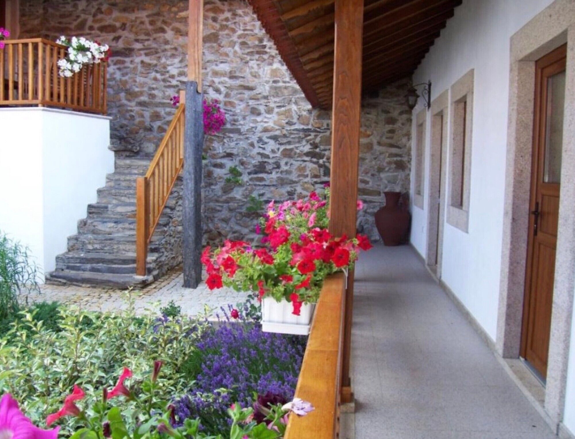 A stone building with a wooden staircase, a flower box with red and pink flowers, and a hallway with wooden doors.