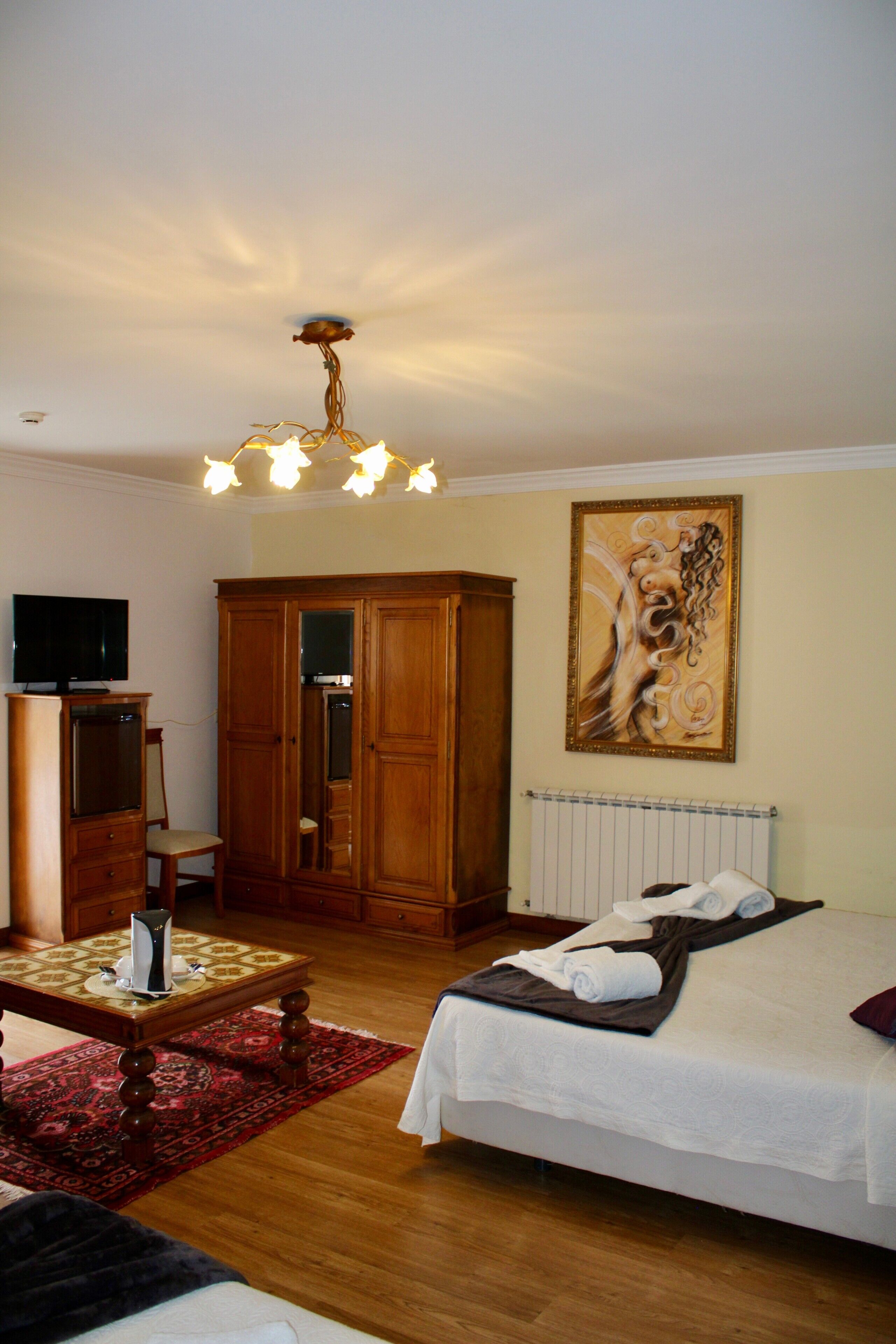 Ein Schlafzimmer mit einem Bett, einem Holzschrank, einem Fernseher auf einem Schrank, einem Bild an der Wand und einer Deckenleuchte.