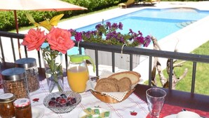 Una mesa con alimentos, un vaso de agua y una taza, frente a una vista de la piscina.