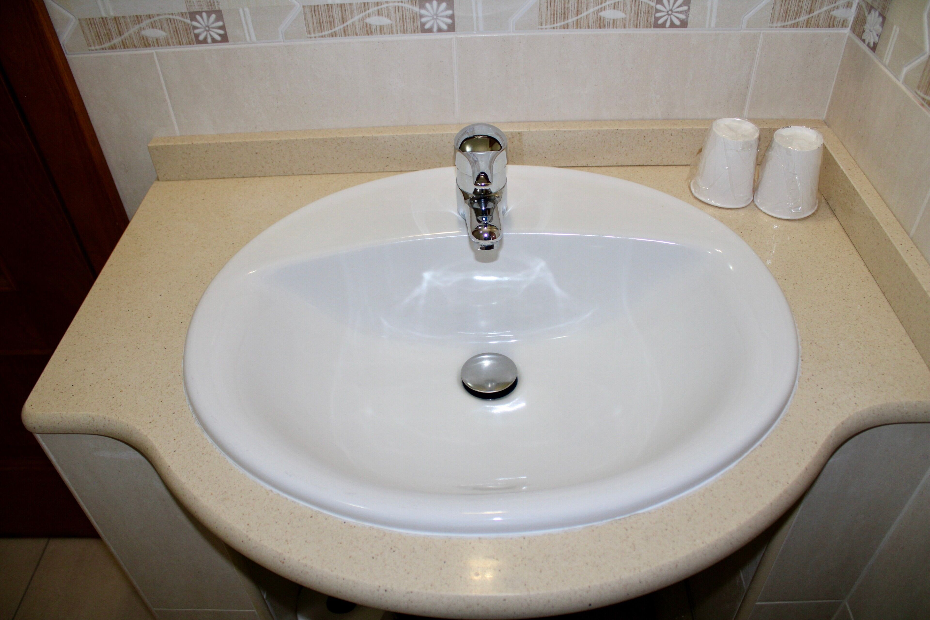 Un lavamanos con grifo, dos tazas y un salpicadero de azulejos.