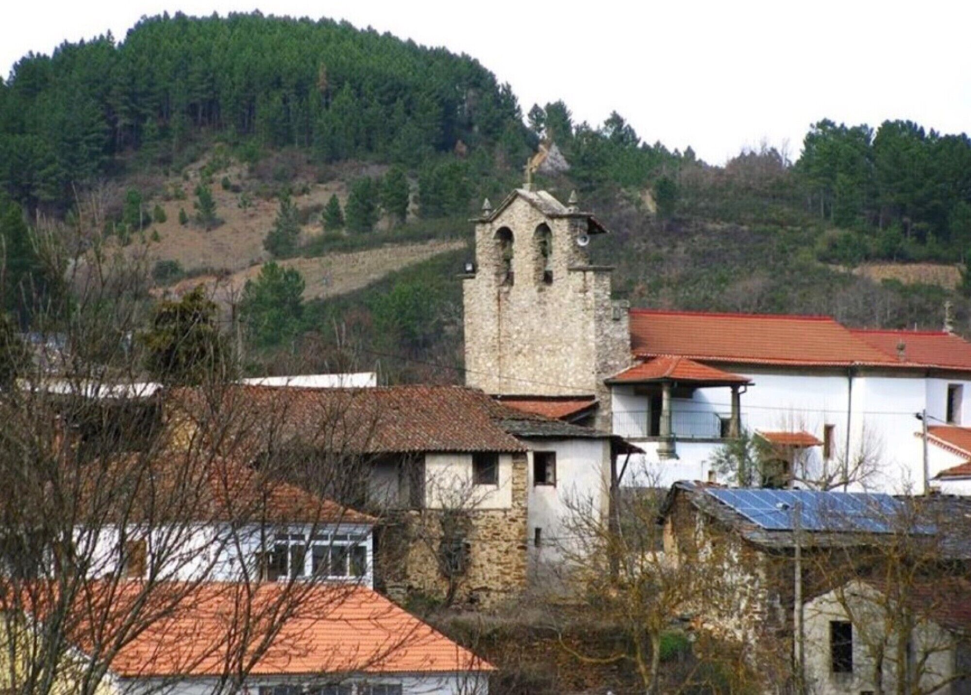 Una iglesia de piedra con un campanario, rodeada de edificios residenciales con tejados rojos.
