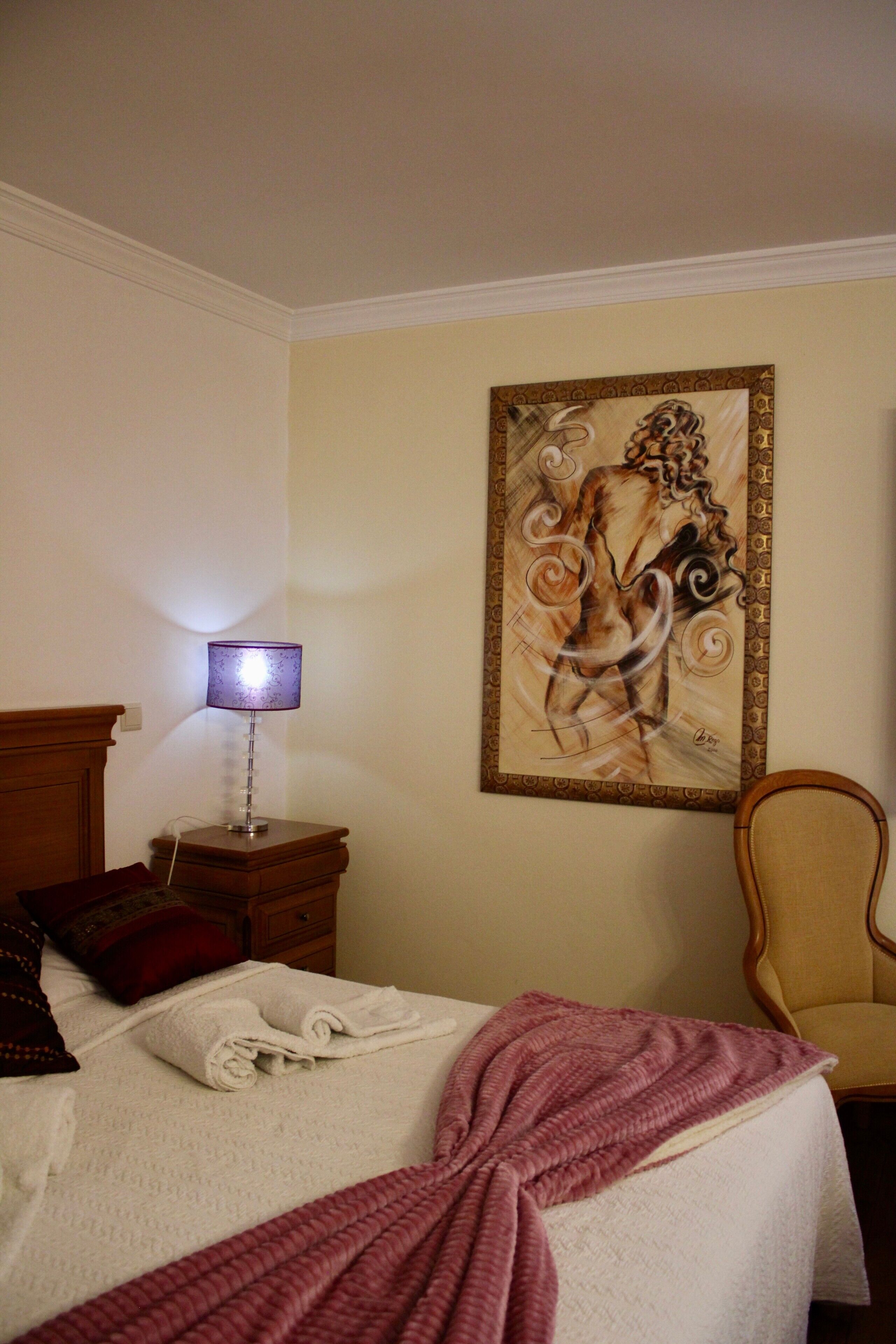 Ein Hotelzimmer mit einem Bett, einem Nachttisch mit Lampe, einem Sessel und einem Wandbild.