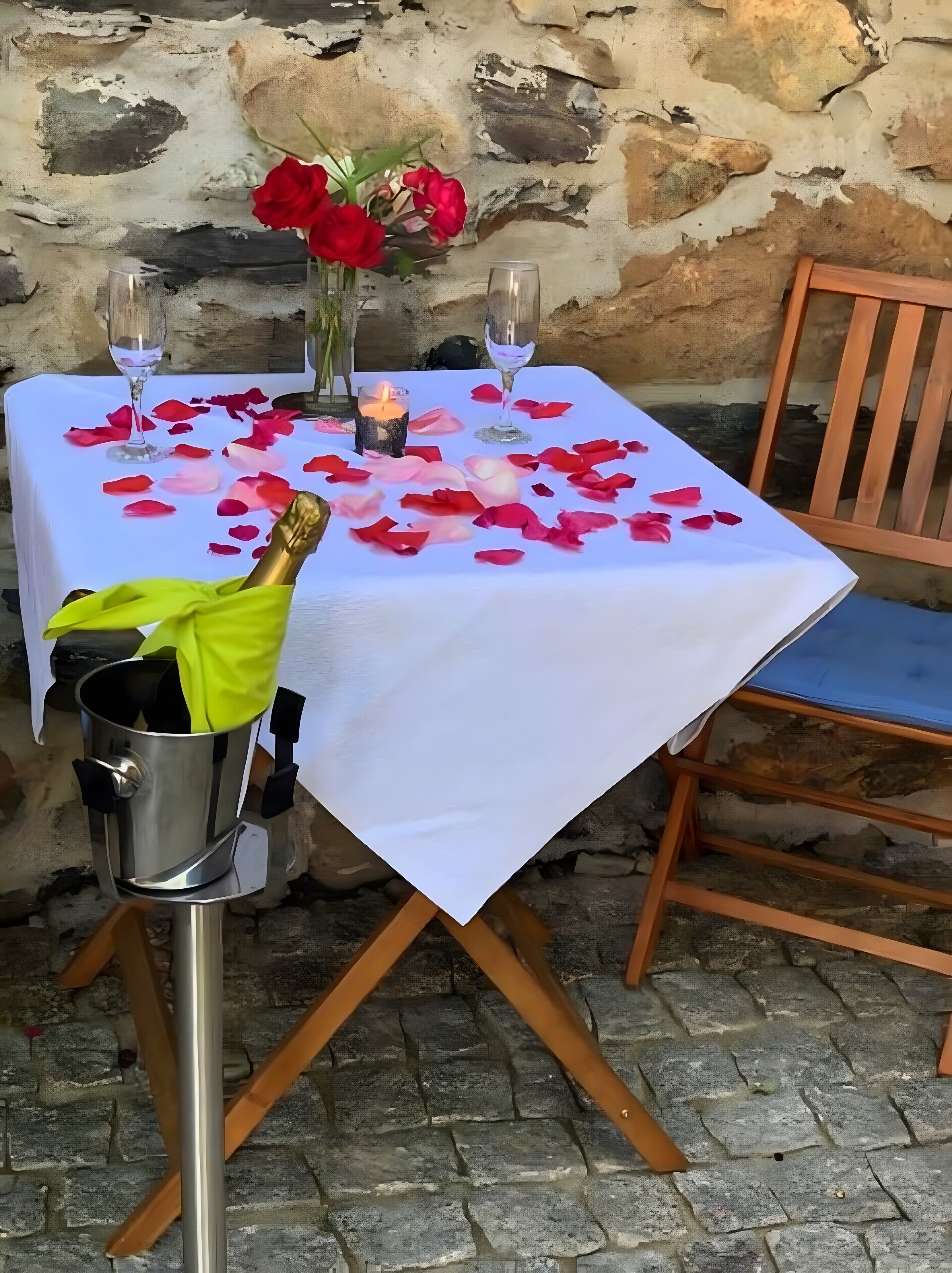 Ein Tisch ist mit einer weißen Tischdecke, Rosenblüten, einer Kerze und einer Champagnerflasche gedeckt.