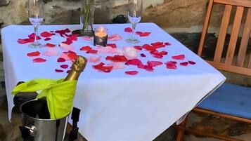 Ein Tisch ist mit einer weißen Tischdecke, Rosenblüten, einer Kerze und einer Champagnerflasche gedeckt.