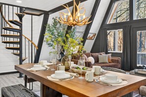 Un comedor con una mesa de madera dispuesta para una comida, una araña y una escalera.