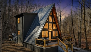 Une cabane dotée d’un toit en pente, de grandes fenêtres et d’une terrasse en bois.