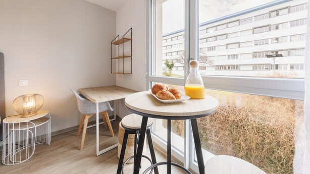 A modern kitchen with a round table, a chair, and a breakfast setup with croissants and orange juice. - 1 Le Loki - Tramway - Wifi (Clermont-Ferrand)