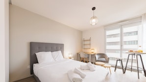 Hotellihuone, jossa on suuri sänky, työpöytä, tuoli, pieni pöytä ja ikkuna, josta on näkymä rakennuksiin.