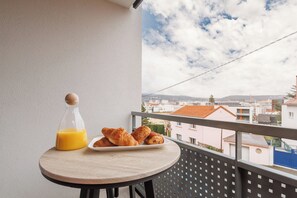 Ein Balkon mit Tisch, gedeckt mit Croissants und einer Orangensaftflasche, mit Blick auf eine Stadtlandschaft.
