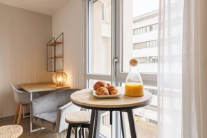 Een moderne kamer met een ronde tafel, een stoel, een lamp, een bord met croissants en een glas sinaasappelsap.