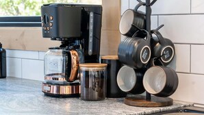Een keuken met een koffiezetapparaat, een glazen kan, een roestvrijstalen container en een kookrek met verschillende pannen en potten.