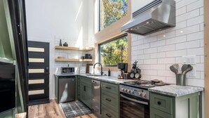 Een moderne keuken met groene kastjes, een ingebouwde magnetron, een fornuis en een groot raam dat voor natuurlijk licht zorgt.