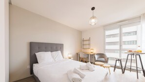 A hotel room with a large bed, a desk, a chair, a small table, and a window with a view of buildings. - 6 Le Loki - Tramway - Wifi (Clermont-Ferrand)