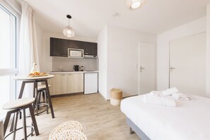 Ein modernes Hotelzimmer mit Bett, einer kleinen Küchenzeile, einem Essbereich und Blick auf die Stadt.