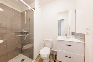 Ein modernes Badezimmer mit einer Duschkabine, einer weißen Toilette und einem Waschbecken mit Spiegel.