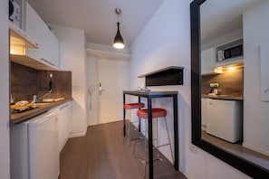 Une cuisine compacte équipée d’un four à micro-ondes, d’un petit réfrigérateur et d’un évier. On y trouve un tabouret de bar et une suspension lumineuse au-dessus du comptoir.