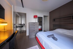 Moderni hotellihuone, jossa on suuri sänky, työpöytä lampun kanssa, vaatekaappi ja punaisella värillä korostettu seinä.