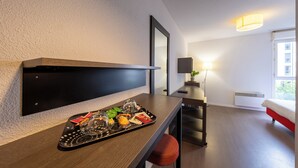 A modern hotel room with a wooden dining table, a tray with snacks and drinks, a red chair, a bed with a red headboard, and a large window with natural light. - 1 - L'Envol - Gare - Wifi (Toulouse)
