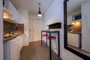 Eine kompakte Küche mit einer Mikrowelle, einem kleinen Kühlschrank und einem Spülbecken. Ein Barhocker und eine Pendelleuchte befinden sich über der Arbeitsfläche.