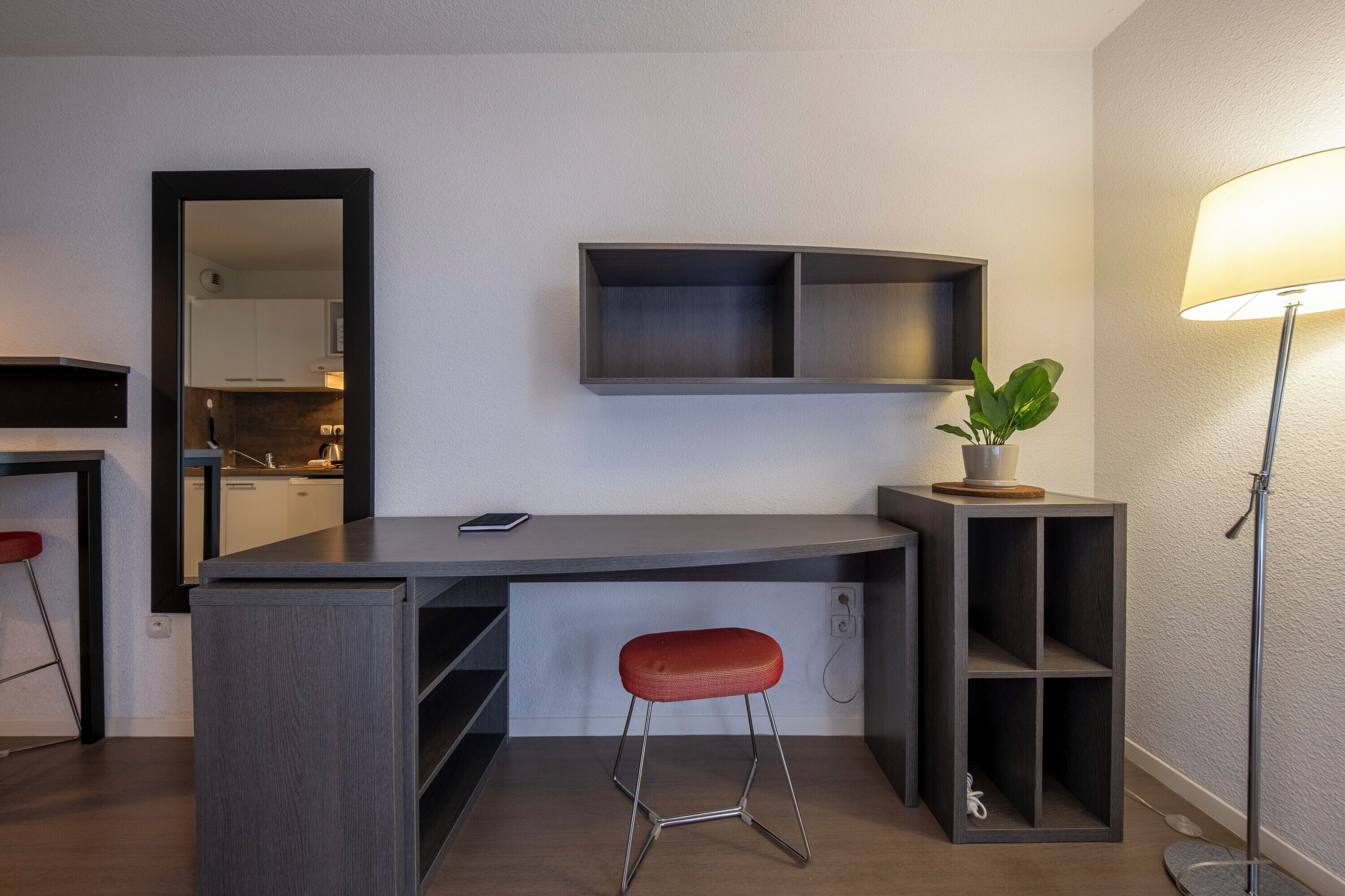 A modern kitchen with a built-in island, a stool, a plant, and a lamp.