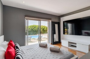 A modern bedroom with a large bed, a TV, and a sliding glass door leading to a pool area.