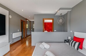 A modern bedroom with a large bed, a red accent wall, and a view into the bathroom.