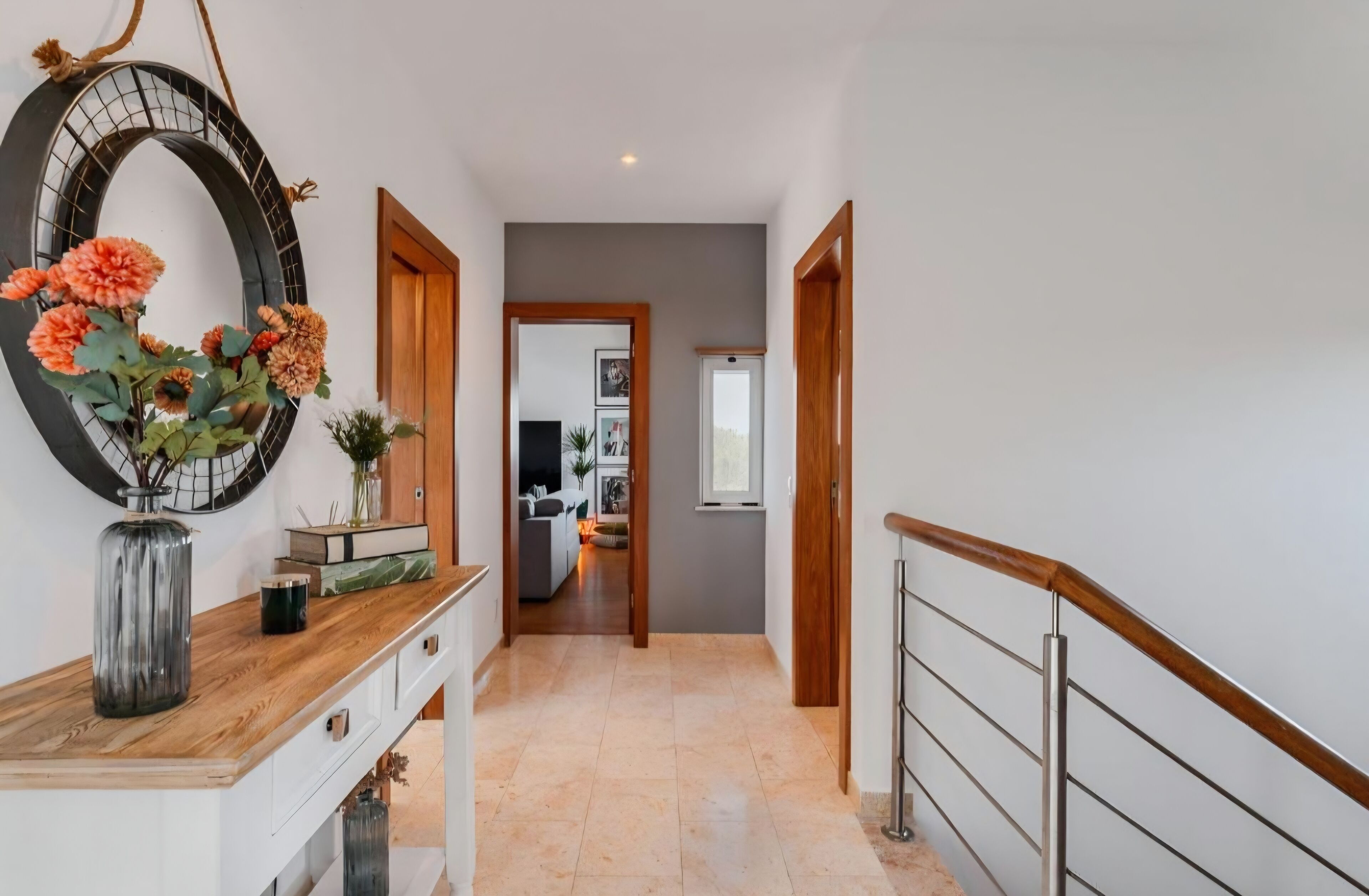 Un couloir avec un bureau en bois, un grand miroir et un vase rempli de fleurs.