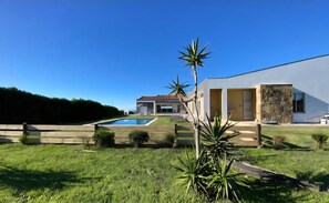A modern house with a swimming pool, a well-maintained lawn, and a large tree in the foreground.