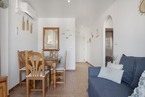 A dining area with wooden chairs and a table, a blue sofa with pillows, and a hallway leading to another room. - Apartamento 'Casa Hinojal' con terraza privada, balcón y aire acondicionado (Conil de la Frontera)