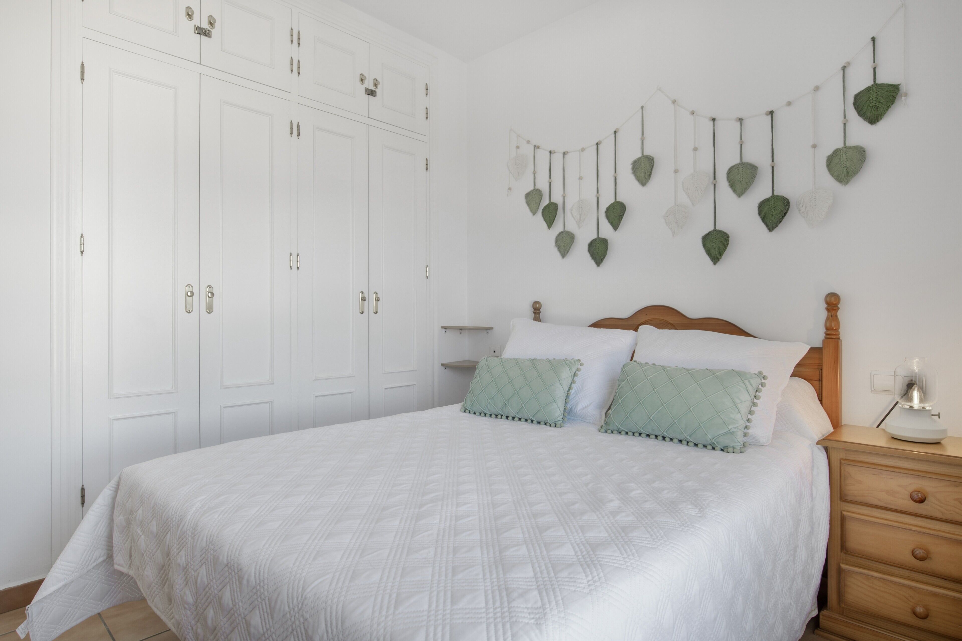 A bedroom with a bed, white wardrobe, and a wall-mounted leaf decoration.