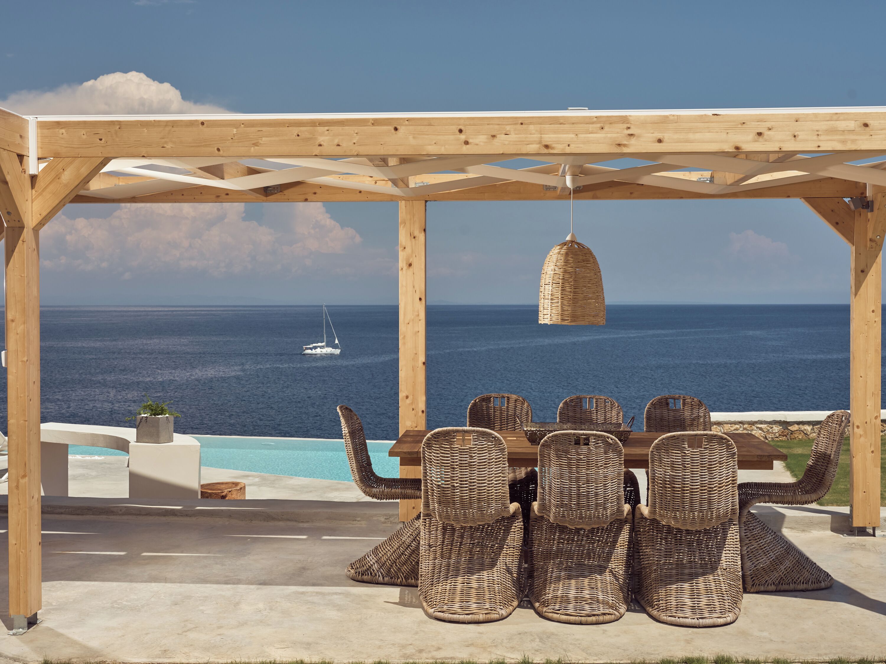 A wooden pergola with wicker chairs overlooking a pool and the ocean.