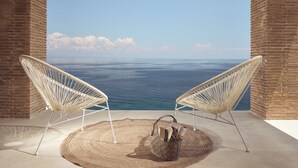 Twee rieten stoelen gericht op uitzicht over de oceaan, een geweven vloerkleed, en een handtas op de vloer.