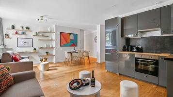 Un salon moderne avec un canapé gris, un coin repas avec une table et des chaises, et une cuisine avec des meubles gris et un four encastré.