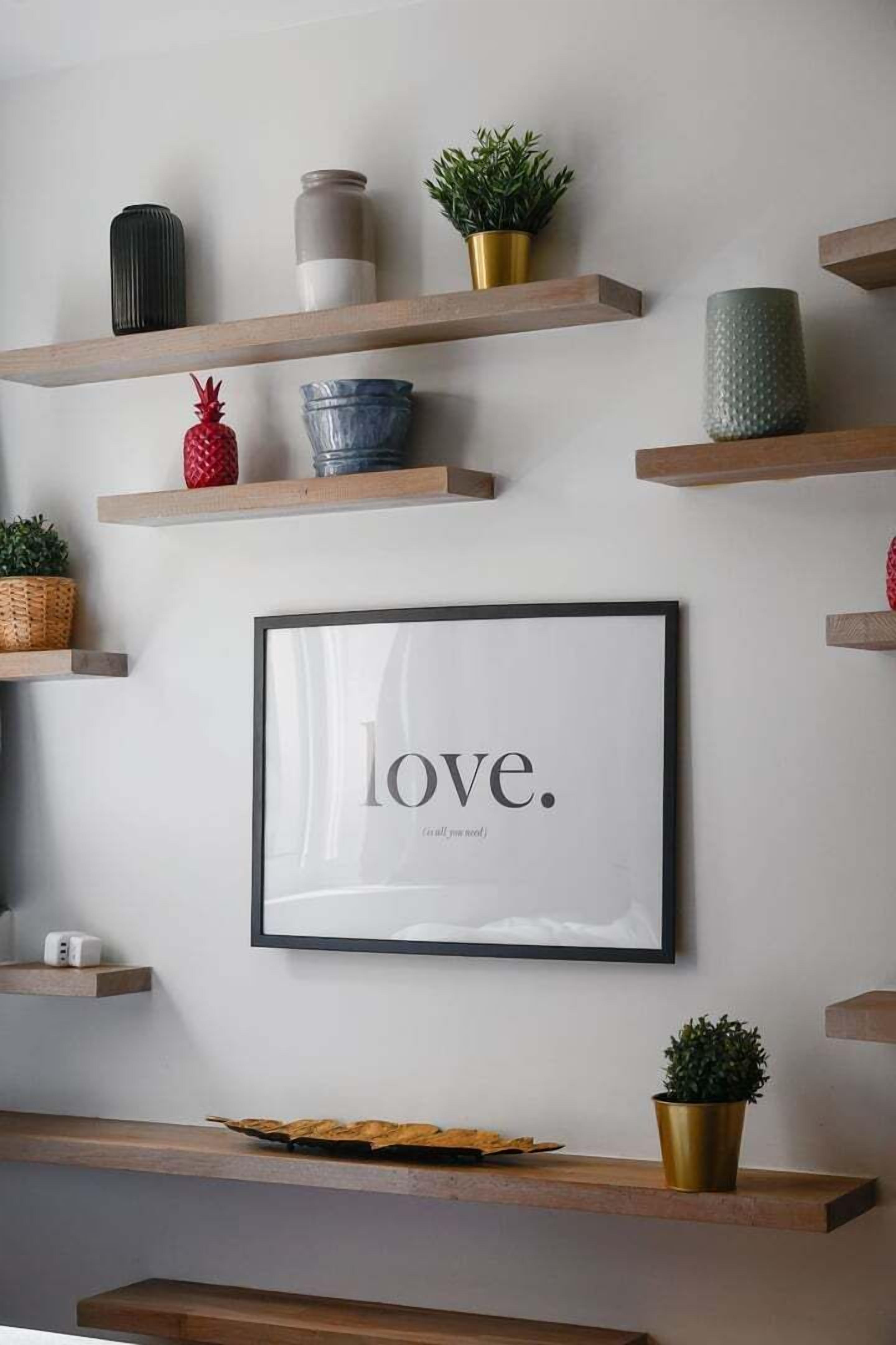 Un mur orné de plusieurs étagères en bois sur lesquelles sont disposés divers objets décoratifs, ainsi qu’un cadre contenant une citation.