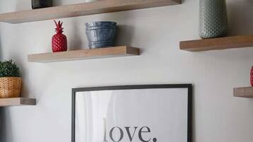 Un mur orné de plusieurs étagères en bois sur lesquelles sont disposés divers objets décoratifs, ainsi qu’un cadre contenant une citation.