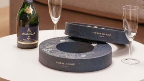 Et rundt bord med en flaske Aguila Brut champagne, to tomme vinglas og en Pierre Hermé chokoladekasse.