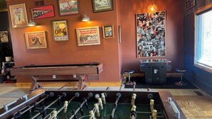 A room with a foosball table, a pool table, and various framed posters on the walls. - Cozy Gem With Stunning Mississippi River View (Albany)