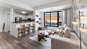 A modern apartment with a kitchen, dining area, and living room. It features a large window, a fireplace, and a cozy seating area. - Solara – Luxury 1BR Downtown (Stamford)