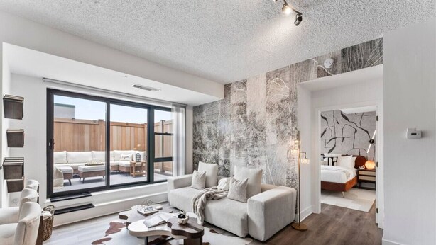 A spacious living room with a large sliding glass door leading to a patio, a cozy seating area with a sofa and armchairs, and a modern art piece on the wall. - Solara – Luxury 1BR Downtown (Stamford)