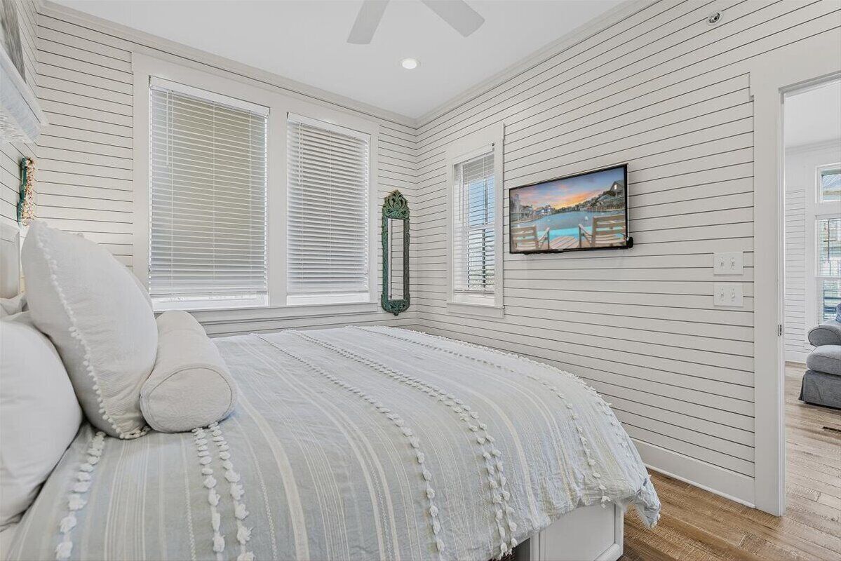 Een slaapkamer met een bed, witte muren, een televisie en een raam met zonwering.