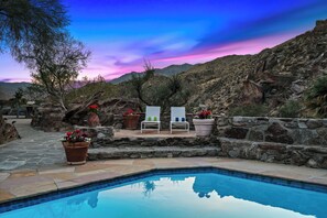 A pool area with two lounge chairs, a stone pathway, and a mountainous backdrop.