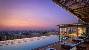 Una piscina a sfioro sul tetto con sedie a sdraio, vista sulla città e una zona riparata con attrezzature per esercizi.
