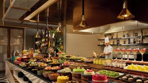 Un buffet con diverse portate, uno chef e una zona cucina ben illuminata.