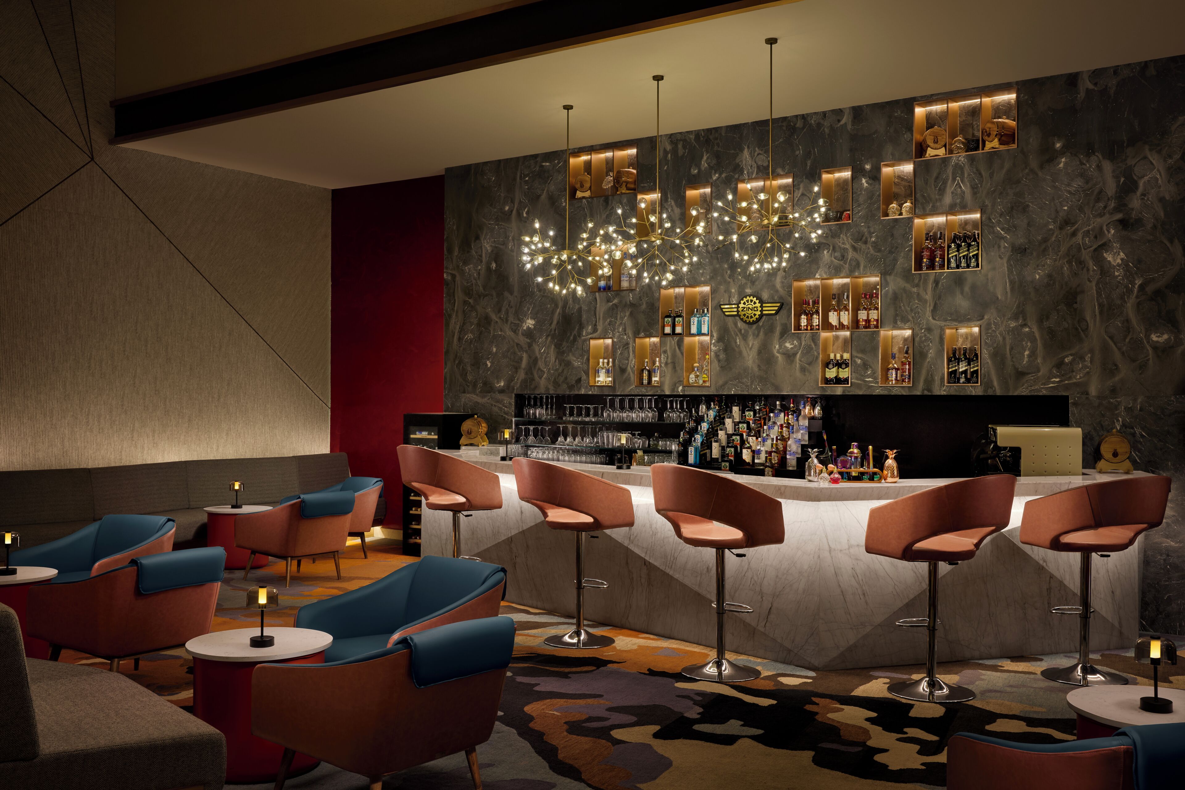 A bar area with seating and a marble wall with illuminated shelves.